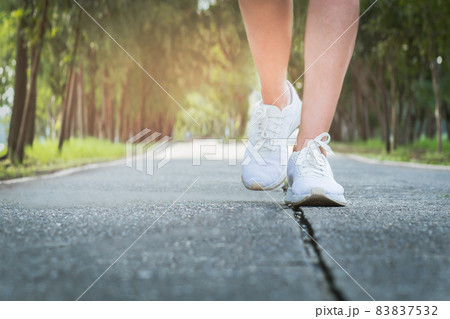 Female exercise walking on street in the park with close up on walking shoes. Female exercise walking on street in the park with close up on walking shoes. 83837532