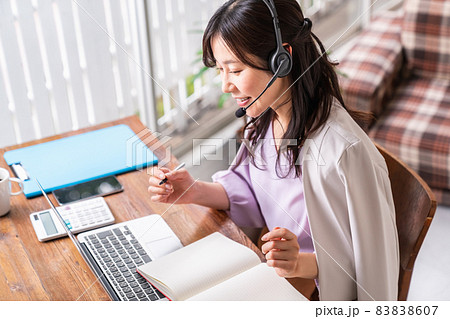 ヘッドセットをつけて筆記用具を持ちノートパソコンと向き合う女性 83838607