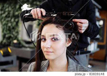 The master does hair styling in a beauty salon. Young woman preparing for a date. 83839148