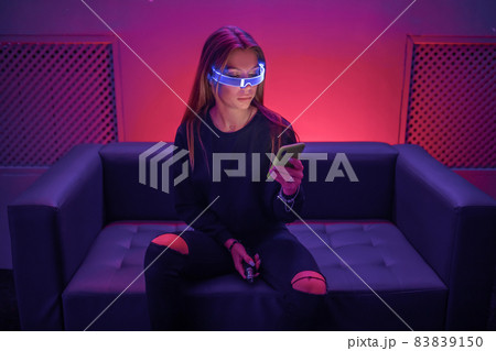 Hipster in neon glasses looks at the phone. Hipster in neon glasses looks at the phone. 83839150