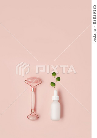 Beautiful composition of white mockup serum bottle, pink quarts stone face roller and fresh leaves on pink background. Natural cosmetics concept. Creative trendy cosmetics flat lay with copy space. Beautiful composition of white mockup serum bottle, pink quarts stone face roller and fresh leaves on pink background. Natural cosmetics concept. Creative trendy cosmetics flat lay with copy space. 83839185