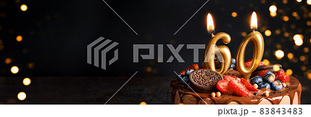 Banner with Chocolate birthday cake with berries, cookies and number sixty golden candles on black background, copy space Banner with Chocolate birthday cake with berries, cookies and number sixty golden candles on black background, copy space 83843483