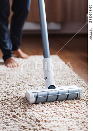 Human legs and a white turbo brush of a cordless vacuum cleaner