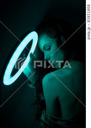 Emotional studio portrait young woman in a wireless headphones with ring flash effect. Round LED Circle Lamp. 83851808