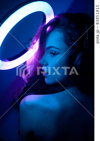 Emotional studio portrait young woman in a wireless headphones with ring flash effect. Round LED Circle Lamp. 83851815