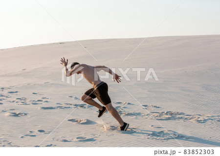 Fit man running fast on the sand. Powerful runner training outdoor on summer. 83852303