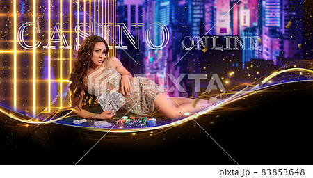 Woman in golden dress. Holding some cash, posing lying on green playing table with stacks of chips, cards on it. Cityscape background. Poker, casino 83853648