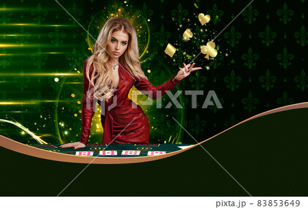 Blonde woman in red dress is showing golden flying suits of cards, leaning on playing table, posing on colorful background. Copy space. Poker, casino 83853649