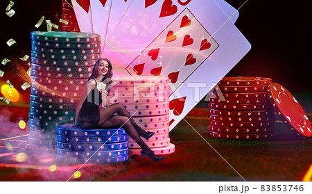 Model is holding two aces, sitting on stacks of chips on green playing table. Colorful background with cards, flying dollars and coins. Poker, casino Model is holding two aces, sitting on stacks of chips on green playing table. Colorful background with cards, flying dollars and coins. Poker, casino 83853746
