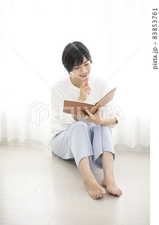 部屋で床に座ってノートを見る女性 83853761