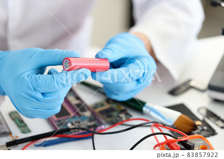 Master holding electronic battery near microchips in workshop closeup 83857922