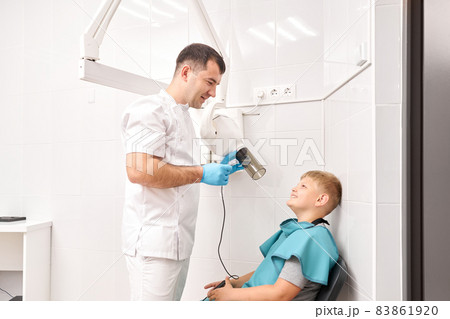 Radiographer taking teeth radiography to a boy using digital x-ray machine in pediatric dental clinic. Dentist prepares boy for tooth x-ray image in dental clinic. Radiographer taking teeth radiography to a boy using digital x-ray machine in pediatric dental clinic. Dentist prepares boy for tooth x-ray image in dental clinic. 83861920