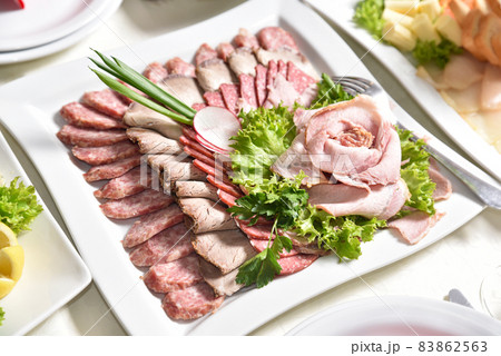 Sliced meat is decorated with greens. Banquet table with delicious food in a restaurant. Professional and exquisite dish serving at restaurant. Catering service 83862563