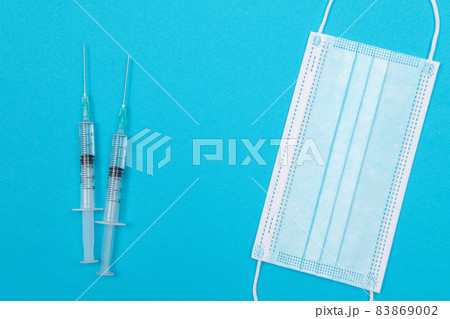 Syringe with Medical Mask on Blue Table - Flat Lay Syringe with Medical Mask on Blue Table - Flat Lay 83869002