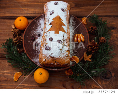 Christmas fruitcake powdered sugar tangerine fir tree festive decoration wooden background flat lay. Stollen cake loaf Christmas fruitcake powdered sugar tangerine fir tree festive decoration wooden background flat lay. Stollen cake loaf 83874124