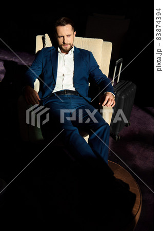 High angle view of a successful young businessman at business trip, relaxing on an armchair with outstretched crossed legs on an ottoman in lounge bar of a luxury hotel High angle view of a successful young businessman at business trip, relaxing on an armchair with outstretched crossed legs on an ottoman in lounge bar of a luxury hotel 83874394