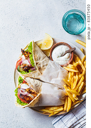 Chicken gyros with vegetables, french fries and tzatziki sauce on plate. Greek food concept. Chicken gyros with vegetables, french fries and tzatziki sauce on plate. Greek food concept. 83875450