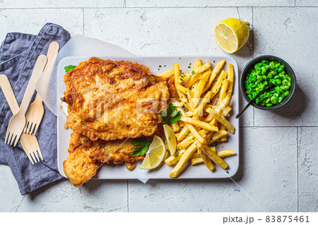 Fish and chips with green peas on gray tile background. British cuisine concept. Fish and chips with green peas on gray tile background. British cuisine concept. 83875461
