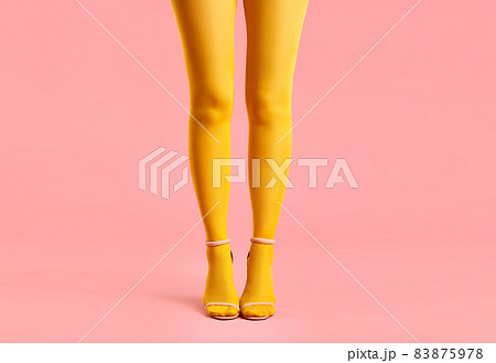 Long slender legs of young woman in yellow tights and stylish high heels shoes on pink background. 83875978