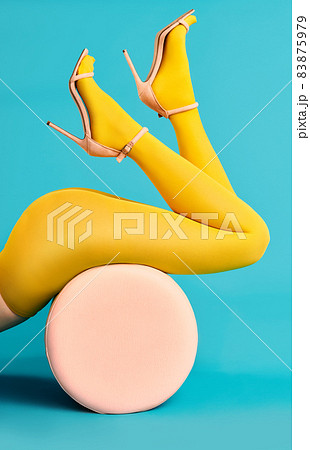 Legs of beautiful young woman wearing bright yellow tights and high heels shoes lying on pouf 83875979