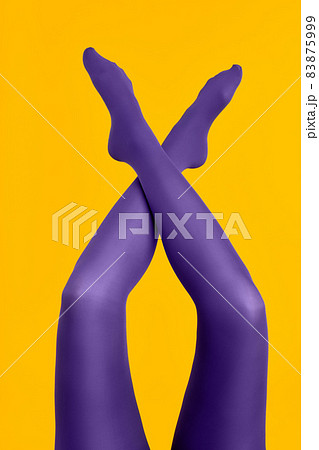 Slim female legs in purple tights raised up on yellow background 83875999