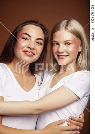 two pretty diverse girls happy posing together: blond and brunette, caucasian and asian on brown background, lifestyle people concept 83876508