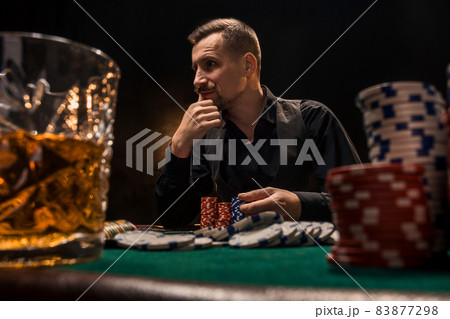 Young handsome man sitting behind poker table with cards and chips Young handsome man sitting behind poker table with cards and chips 83877298
