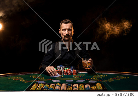 Poker player. Young guy in the casino at the gaming table. Man gambling, card games. Cards, chips, whiskey, cigarettes, poker, card game, gambling - gambling concept. Poker player. Young guy in the casino at the gaming table. Man gambling, card games. Cards, chips, whiskey, cigarettes, poker, card game, gambling - gambling concept. 83877380