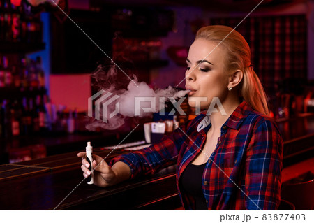 Young pretty woman smoke an electronic cigarette at the vape bar 83877403