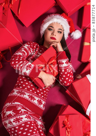Funny young woman in a New Year's dress lying on a mountain of gifts. 83877714