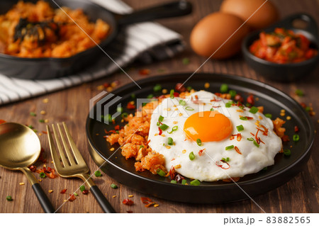 Kimchi Fried rice topped with fried egg and fresh kimchi cabbage in a bowl on placed wooden background. Korean food style Kimchi Fried rice topped with fried egg and fresh kimchi cabbage in a bowl on placed wooden background. Korean food style 83882565