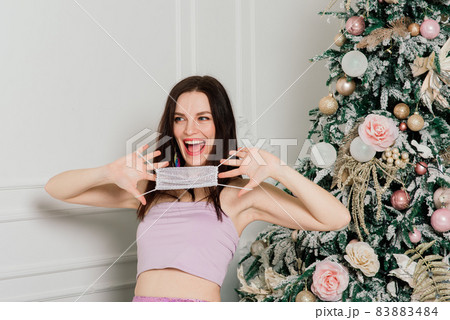 Young beautiful European woman in medical mask with holiday gifts at home, quarantine coronavirus. Young beautiful European woman in medical mask with holiday gifts at home, quarantine coronavirus. 83883484