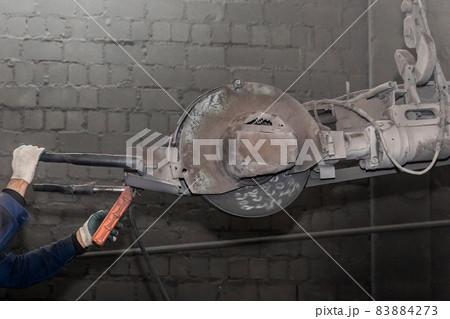 A hand's of a man controls heavy equipment with grinding stone to clean reinforced concrete structures in a workshop of an industrial plant A hand's of a man controls heavy equipment with grinding stone to clean reinforced concrete structures in a workshop of an industrial plant 83884273