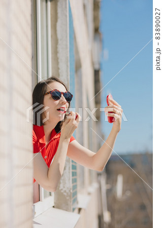 a pretty woman in a red dress looks out the window of her house 83890027