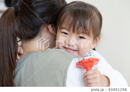 自宅のリビングでママに抱っこされて笑う2歳の女の子の写真素材