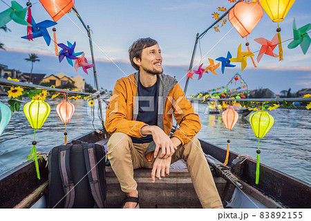 Happy man traveler ride a national boat on background of Hoi An ancient town, Vietnam. Vietnam opens to tourists again after quarantine Coronovirus COVID 19 83892155
