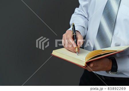 Businessman makes notes in a notebook with a fountain pen. Writes startup business ideas, plans, creative thoughts to notebook. close up. Makes appointment notes time. on a gray background. copy space 83892269