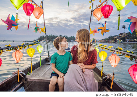 Happy family Mother and son of travelers ride a national boat on background of Hoi An ancient town, Vietnam. Vietnam opens to tourists again after quarantine Coronovirus COVID 19 83894049
