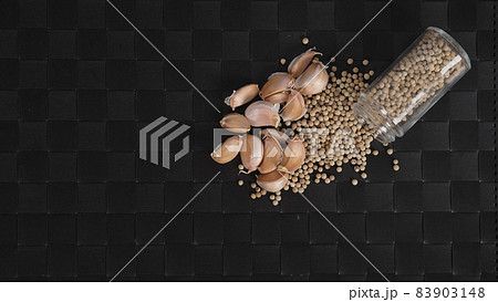 Garlic and pepper. Natural Garlics and white peppercorn in glass bottle on plate mat black background. Ingredient for many World food recipe. Represent to hot and spicy of spice of Garlic and pepper. 83903148