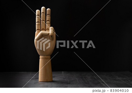 Picture of a wooden hand showing hand signal. The hand is placed on a wooden table with black background Picture of a wooden hand showing hand signal. The hand is placed on a wooden table with black background 83904010