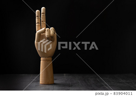 Picture of a wooden hand showing hand signal. The hand is placed on a wooden table with black background 83904011