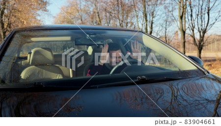 Emotional man in car, view through windshield. Aggressive driving behavior. Angry man driver hitting the steering wheel with his fists. 83904661