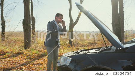 Desperate businessman standing and speak on phone near the broken car opened the hood road help repair stress problem emergency. Desperate businessman standing and speak on phone near the broken car opened the hood road help repair stress problem emergency. 83904754