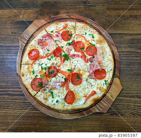 Homemade pizza with tomato, basil, pepperoni and ham on a wooden baking sheet Homemade pizza with tomato, basil, pepperoni and ham on a wooden baking sheet 83905397