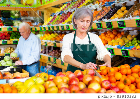 Woman merchandiser in apron putting goods on shelf in supermarket 83910332
