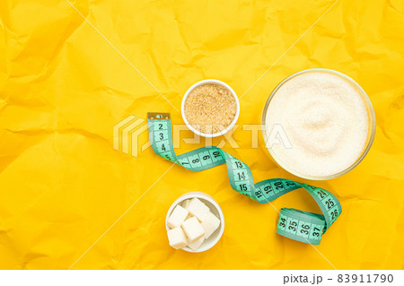 Different types of sugar and diet measuring tape on yellow background with copy space. Weight control, healthy food, diet. 83911790