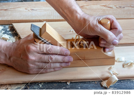 Men's hands hold a wooden jointer close-up. Light wood boards, shavings, sawdust Men's hands hold a wooden jointer close-up. Light wood boards, shavings, sawdust 83912986