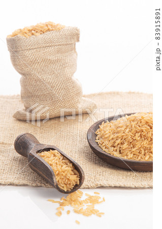 Brown rice on wooden plate and spoon and burlap sack on white backround. 83915891