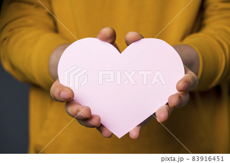 A young man in a casual yellow sweater holds a tender pink romantic heart. 83916451