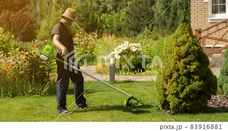 A young man with a lawnmower cares for the grass in the backyard. 83916881